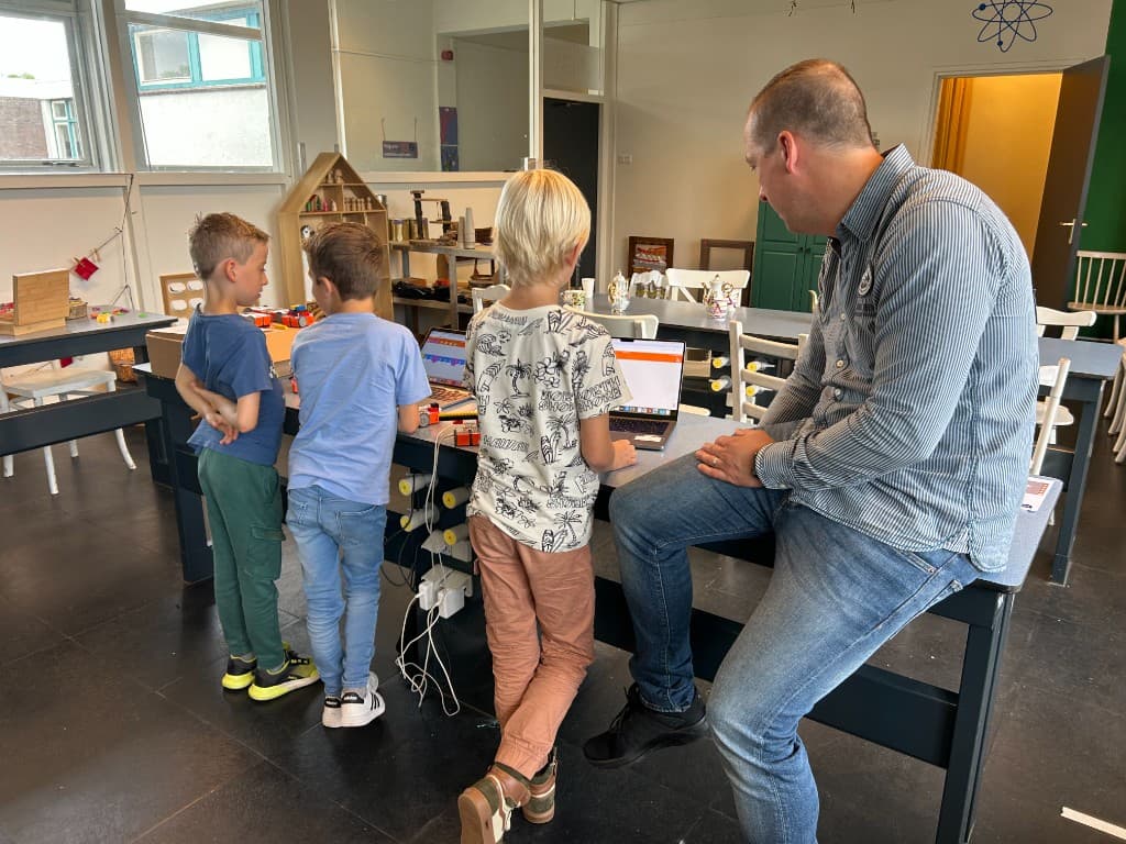 Kinderen en een begeleider bij een BSO werken samen op laptops tijdens een ZelfTech-activiteit